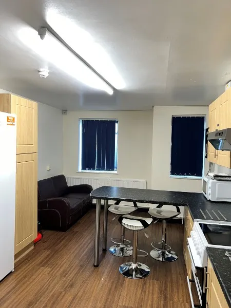 Kitchen in ensuite accommodation at City Campus, a sofa facing a flat television on the wall next to a side table with a microwave and two windows with blue blinds