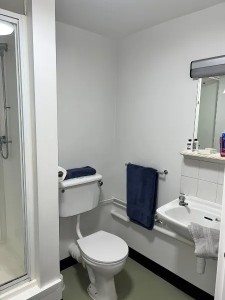 A bathroom in City Campus Ensuite accommodation: a toilet, sink and mirror, towel rail and shower.