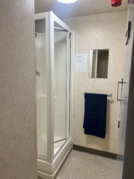 A bathroom in standard accommodation: a shower unit with an accompanying laminated guide on the wall and a towel rail