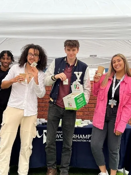 A group of students standing under a tent shelter holding a box of PG Tips teabags