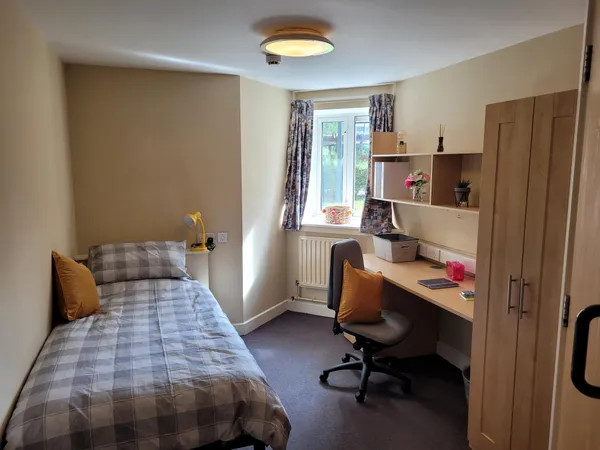 Photograph of a bedroom in Walsall Campus accommodation: A single bed adjacent to a desk, an arrangement of shelves, a cupboard and a window looking outside.