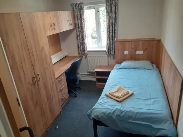 Photograph of an ensuite bedroom in Walsall Campus accommodation: a single bed opposite a desk with attached cupboards and drawers, with a door leading to an attached bathroom.