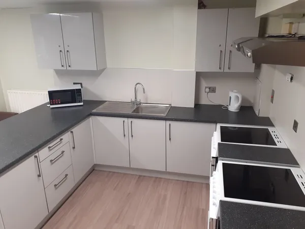 Photograph of a communal kitchen in Walsall Campus accommodation: a countertop with a microwave and kettle, rows of cupboards and two ovens with extractor fans.