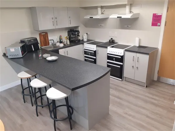 Photograph of a communal kitchen in Walsall Campus accommodation: four chairs seated at a countertop attached to a row of cupboards and ovens.