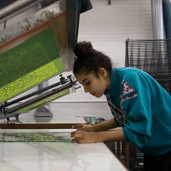 Female student seting up for print on a screen bed in the the screen printing studio.
