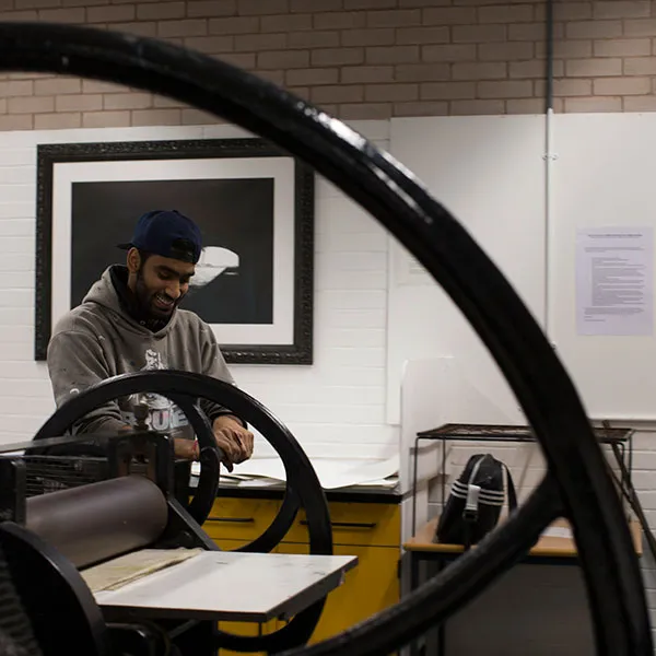 Male student turning the handle on one of the etching presses in the Intaglio print room