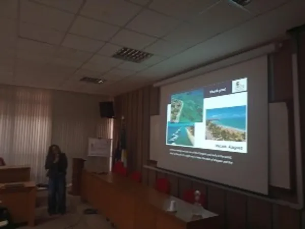 A lecturer speaking in front of an interactive whiteboard, showing images of Macieó, Alagoas