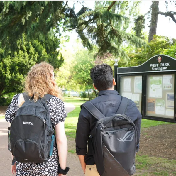 Two people wearing rucksacks and looking at the sign for West Park as they walk along the path