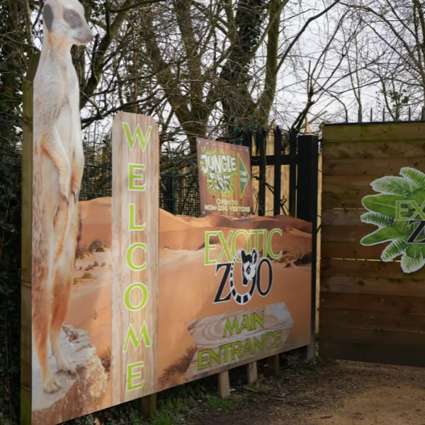 The entrance to Exotic Zoo, a board reading WELCOME bordered by a photo of a meerkat
