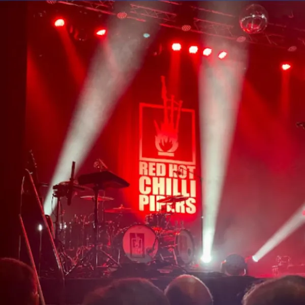 Photo of a Red Hot Chilli Peppers performance at Telford Theatre: a drum set with RHCP decal stickers, the stage lit up with red lights