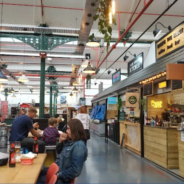 Inside Wellington Market, customers sitting at wooden tables with food and drinks from nearby carts