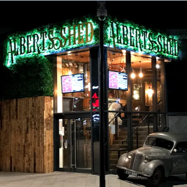 Alberts Shed nightclub, a staircase to an upper floor visible through glass doors, green neon signs identifying the venue, a vintage car parked outside the building
