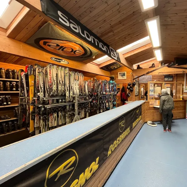 The counter in Telford Snowboard and Ski Centre: boards, boots and skis arranged on the wooden wall behind the counter, various ski and snowboard brand logos displayed on pinned flags