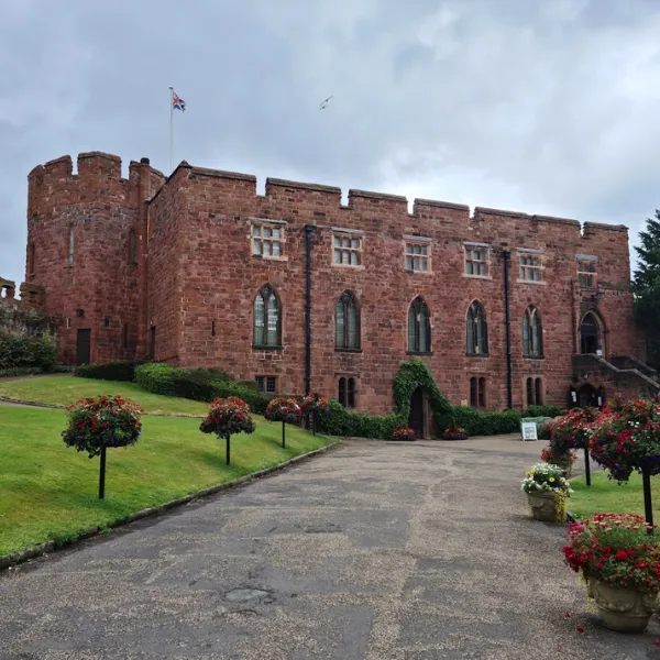 Shrewsbury Castle: a wide footpath leading to an entrance bordered by foliage, tall ramparts and a union flag flying above the walls