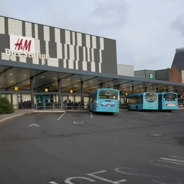 Telford Bus Station with three light blue buses parked outside it, a large H and M logo on the side of the building