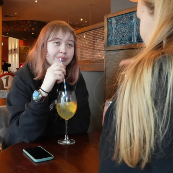 Two students at a table in The Waterfront pub restaurant, one drinking a glass through a paper straw