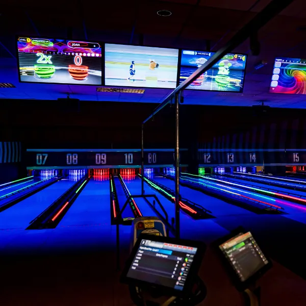 A ten-pin bowling alley: a row of lanes under dark blue lights with the pins illuminated in brighter blues and reds