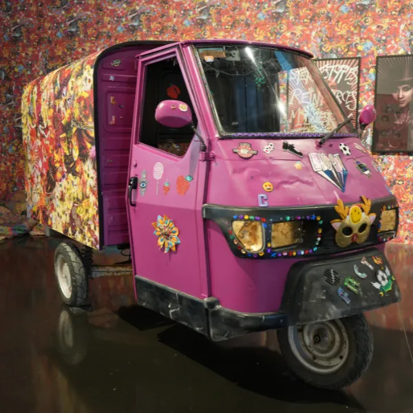 A pink three-wheeled trailer van with a variety of decals on display in the New Art Gallery