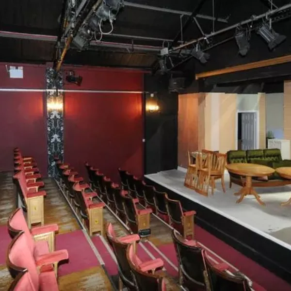 Inside The Grange Playhouse, rows of seats on descending stairs facing a stage decorated to look like a living room