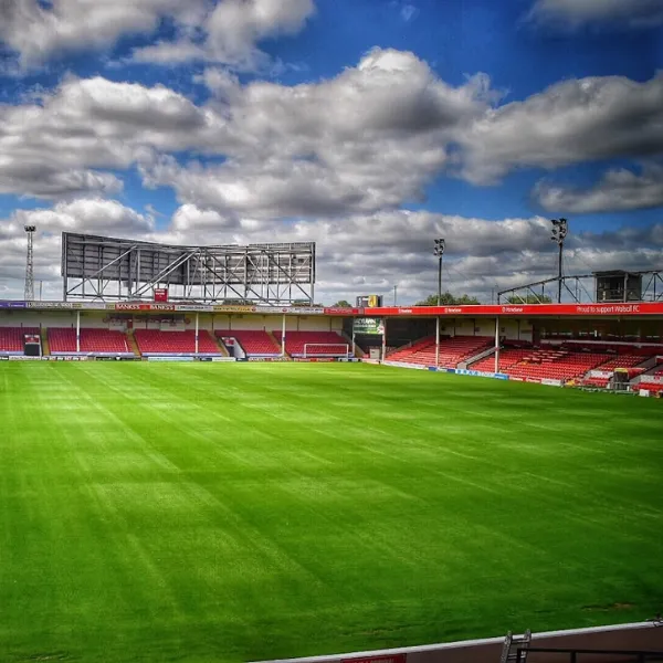 Bescot Stadium football pitch, green grass and a blue sky with grey clouds, rows of seats coloured red
