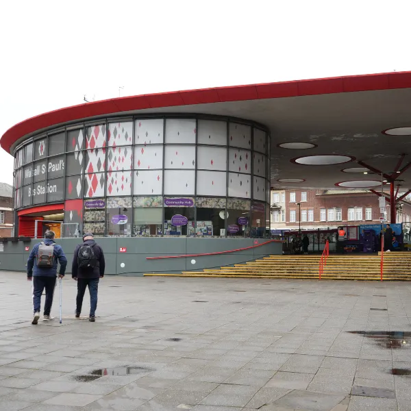 Two people walking towards Walsall St Pauls Bus Station, a round building with a wide, extended roof and its name written across several divided windows