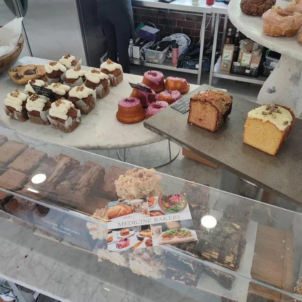 A display of various cakes and sweets at Medicine Bakery, the business title visible on a flyer with the display