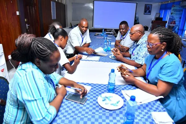 Photograph of eight people seated at a table, taking shared notes on a large sheet of paper.