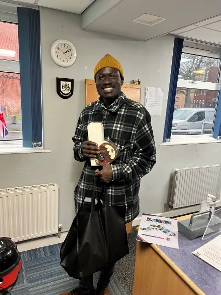 A student in an office room holding a bag and a large cookie stylised as a Christmas pudding