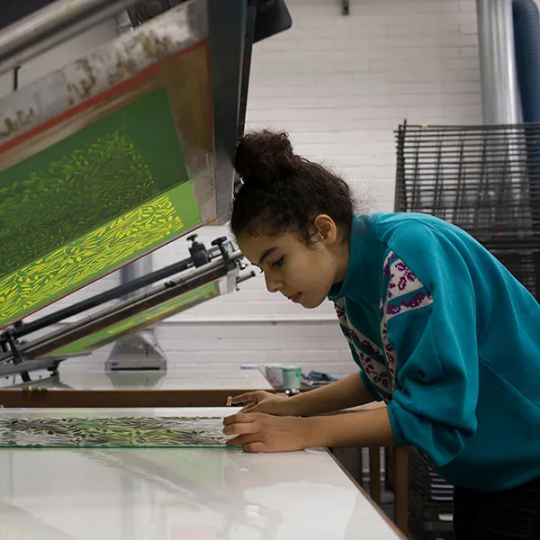 Female student setting up for print on a screen bed in the the screen printing studio.