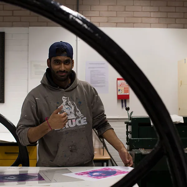Male student looking at a print they have produced using the large etching press in the Intaglio print room