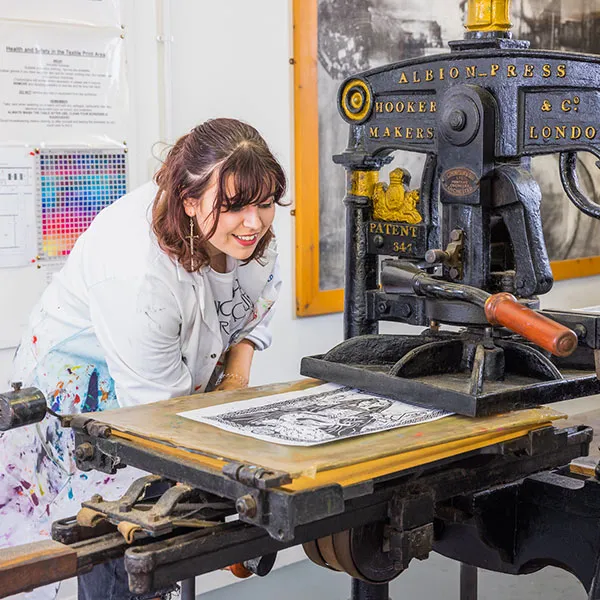 Female student using the small printing press to print a linocut in the Relief printing room