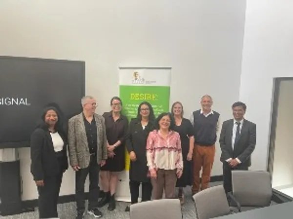 DESIRE project participants standing in a line in front of an inactive interactive whiteboard and DESIRE project signage