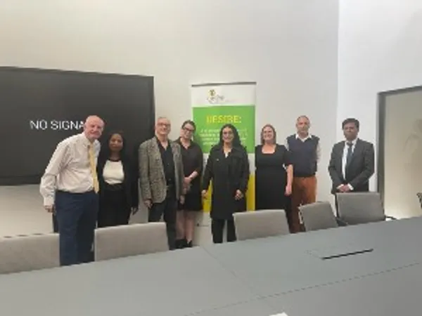 DESIRE project participants standing in a line in front of an inactive interactive whiteboard and DESIRE project signage