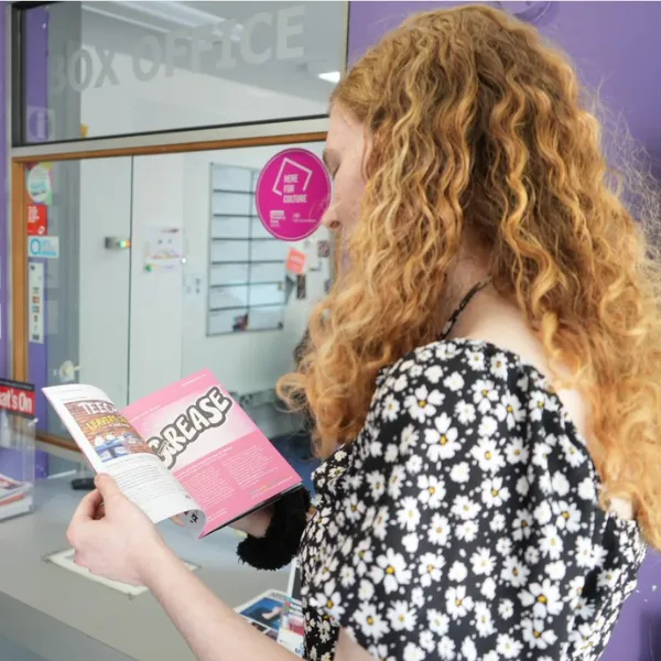 A student outside the box office at the Arena Theatre and looking through the programme