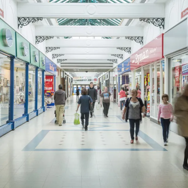 Shoppers walking down a corridor in Telford Centre, storefronts including Shoezone and Ryman on either side of the corridor