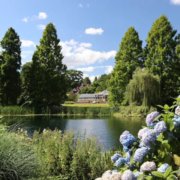 Weston Park House surrounded by gardens: grass, trees and flowers, with a large pond some distance away from the house