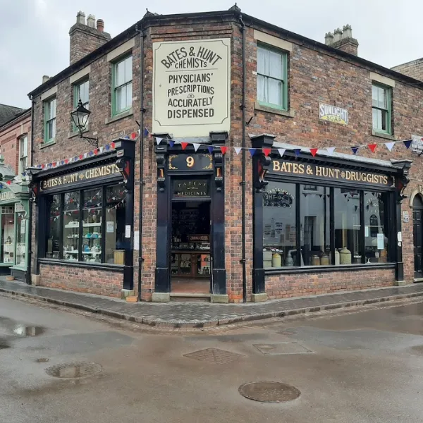 A building in Blists Hill Victorian Town, identified by antiquated storefront signage as BATES AND HUNT CHEMISTS, red, white and blue bunting hanging across the street outside
