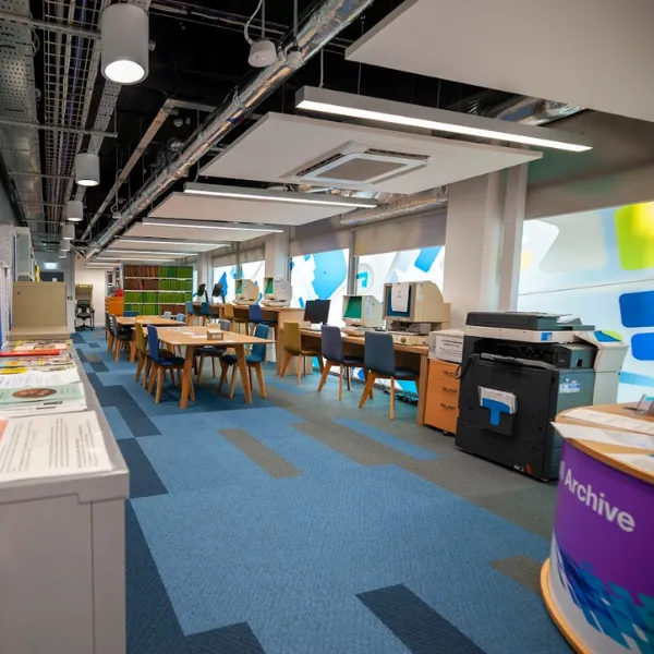 Interior of Walsall Archives: desks, chairs and large desktop computers arranged in a room with a square-patterned blue carpet